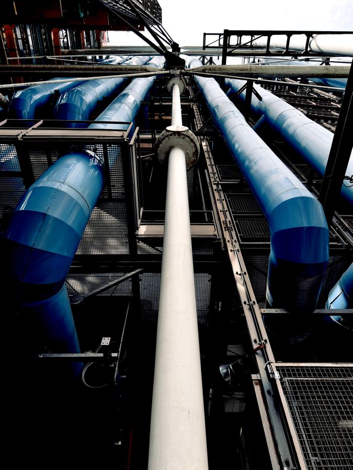 Dramatic view of industrial pipes and blue tubes against sky.